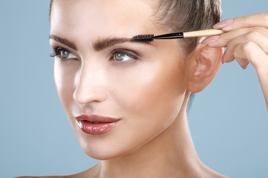 Closeup beautiful woman with eyebrow brush tool on blue